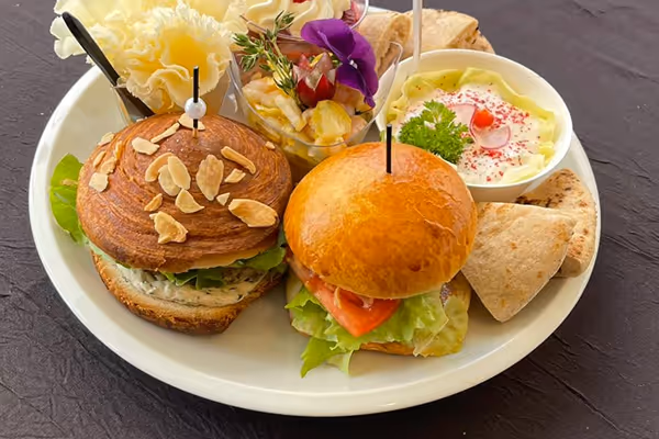 Assiette avec deux petits burgers, une trempette avec du persil, des chips de pita et une salade décorée d'une fleur comestible.