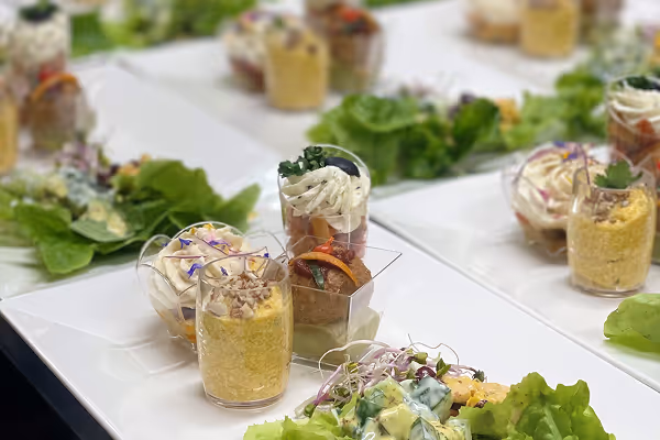 Verres individuels de bouchées apéritives variées présentés sur une assiette blanche avec des feuilles de salade verte en décor.
