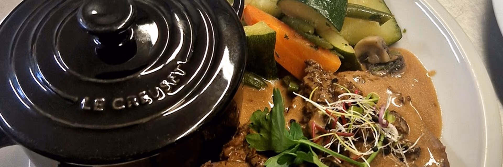 Plat de viande en sauce avec légumes variés, servi à côté d'une cocotte noire Le Creuset.