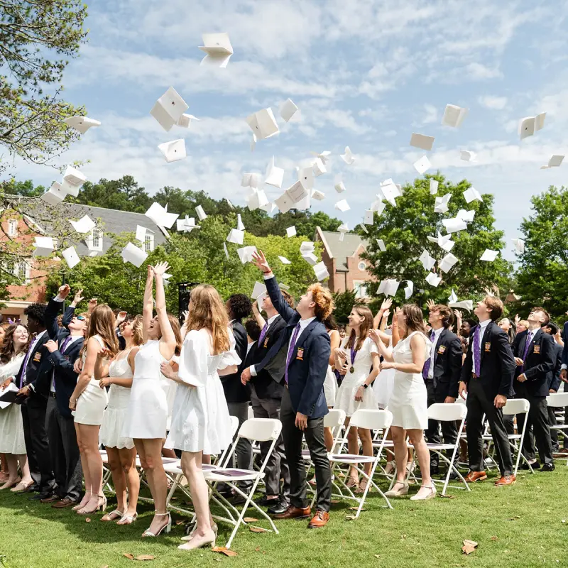 Group of graduates outdoors tossing their caps in the air during a graduation ceremony on a sunny day.