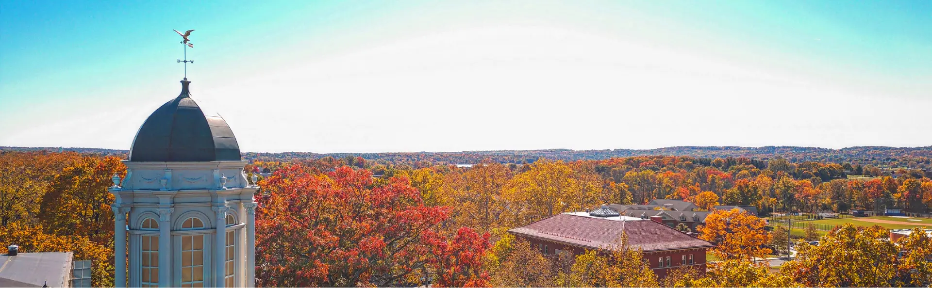 Scenic autumn view with colorful orange and red trees and a historic building topped with a dome and weather vane.