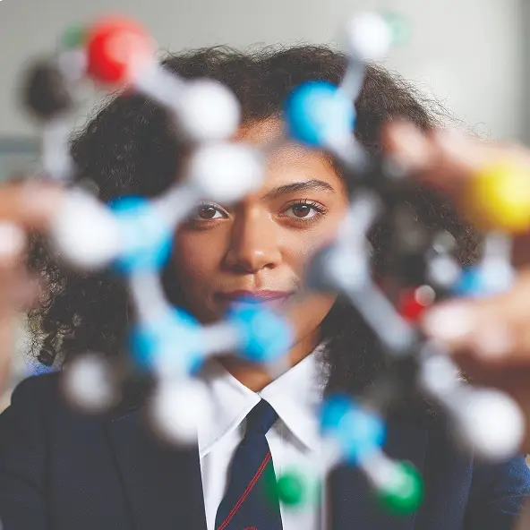 Young person with curly hair intently examining a colorful molecular model in a science setting.