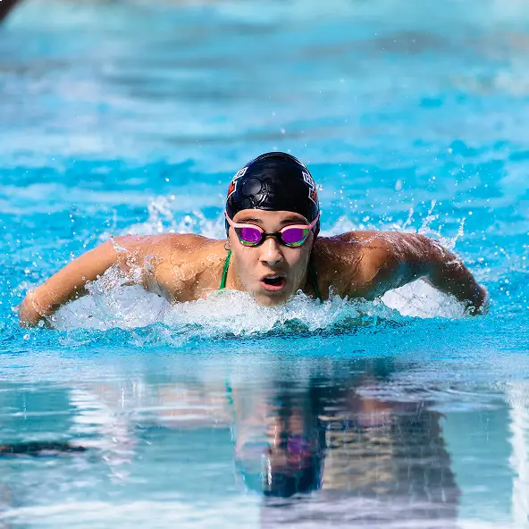 Swimmer wearing black swim cap and purple goggles performing butterfly stroke in pool.
