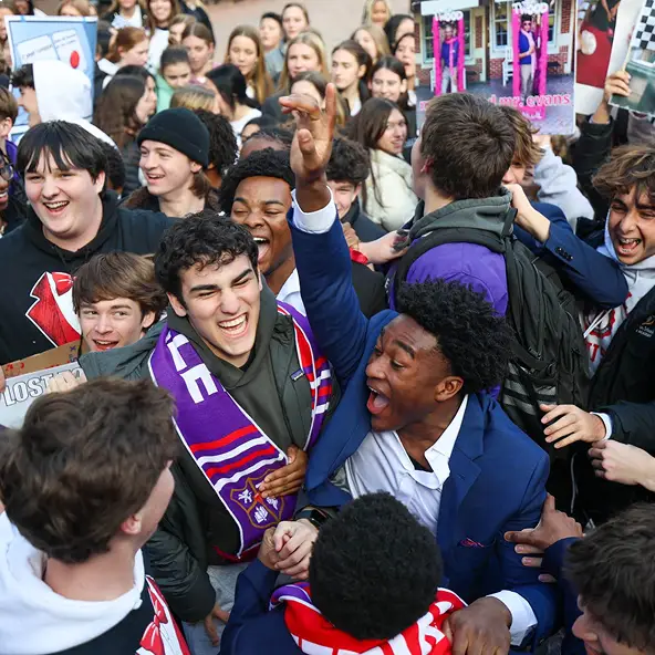 Group of excited teenagers celebrating outdoors, some wearing sports scarves and holding signs.