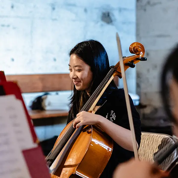 A woman playing the cello with a smile in a rehearsal setting.