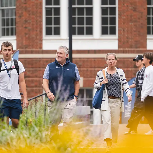 A group of adults and a young man walking outdoors near a brick building with windows.