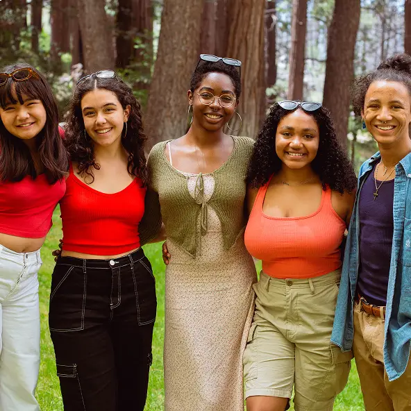 Group of five young diverse friends smiling together outdoors in a wooded area.