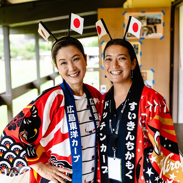 Two smiling women wearing traditional Japanese happi coats and headbands with small Japanese flags.