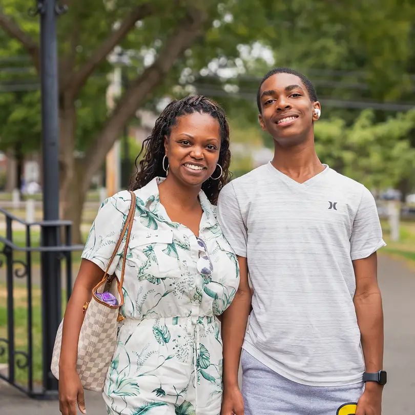 Smiling woman and teenage boy standing outdoors on a pathway with trees in the background.