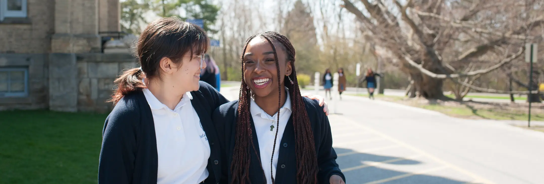 Two smiling students walking outdoors, with one student’s arm around the other in a friendly gesture.
