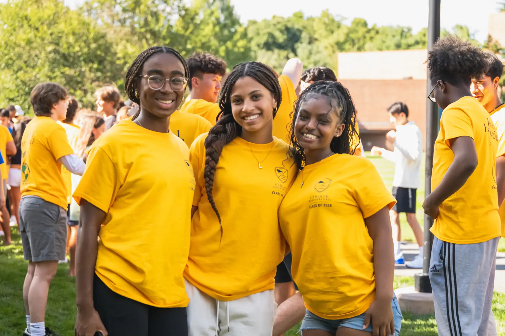 Three young women wearing yellow class of 2026 t-shirts smiling outdoors at a group event.