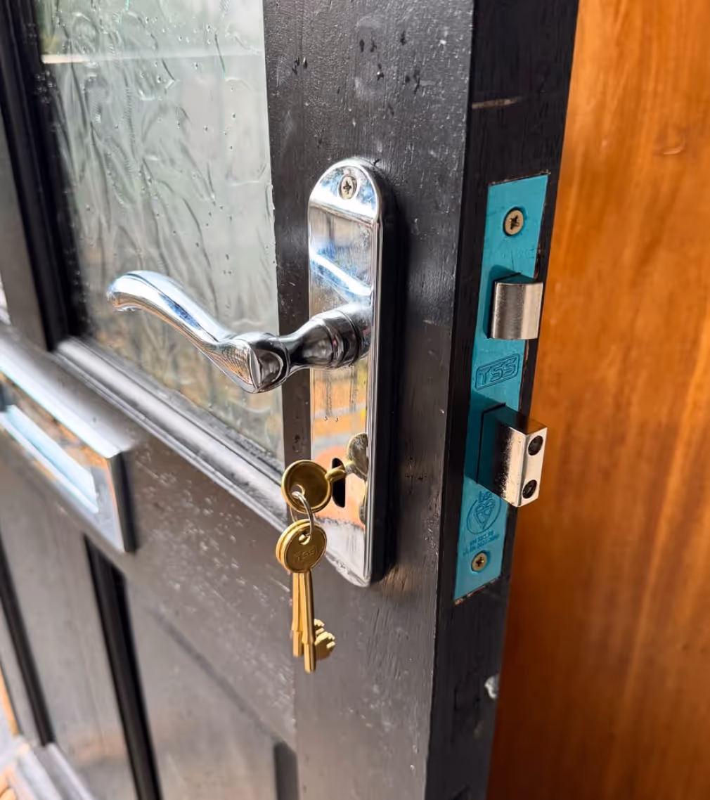 Close-up of a black door with a chrome handle and a keyring holding three brass keys inserted in the lock.