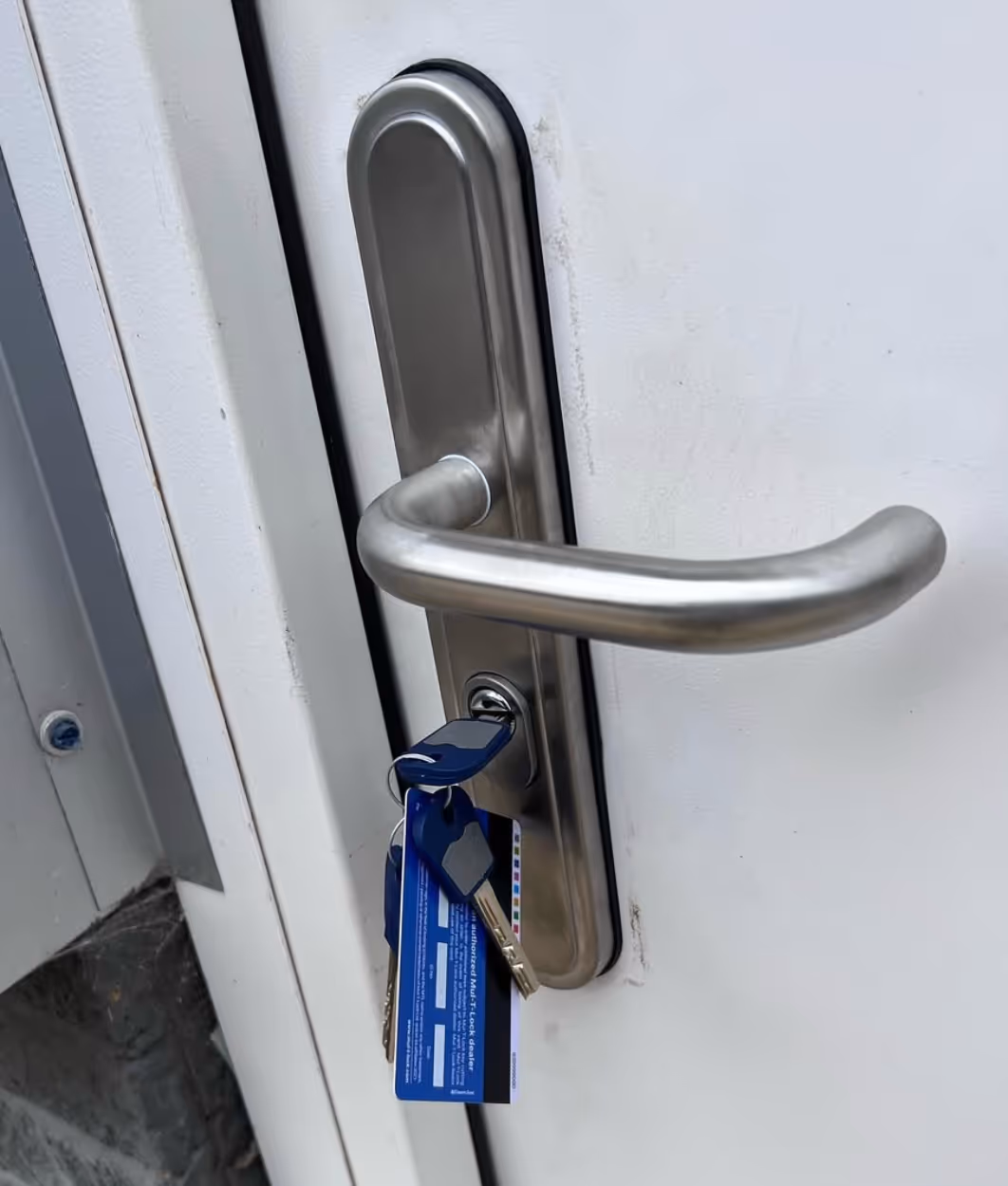 Silver door handle with a key inserted in the lock holding a set of keys and blue key tags attached.
