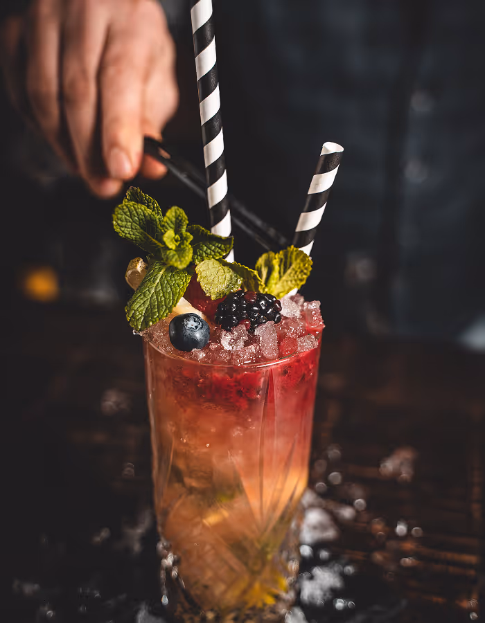 Erfrischender Cocktail mit zerstoßenem Eis, Minzblättern, einer Brombeere und einem Blaubeere mit zwei schwarz-weißen Strohhalmen.