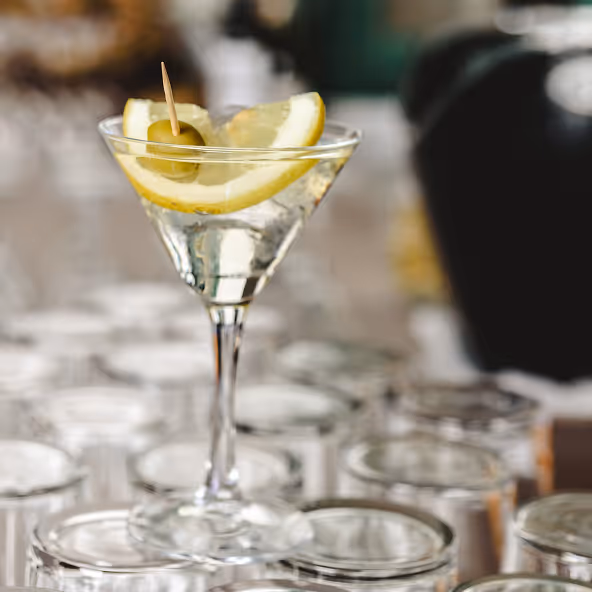 Martiniglas mit klarer Flüssigkeit, garniert mit einem Zitronenschnitz und einer grünen Olive auf einem Zahnstocher.