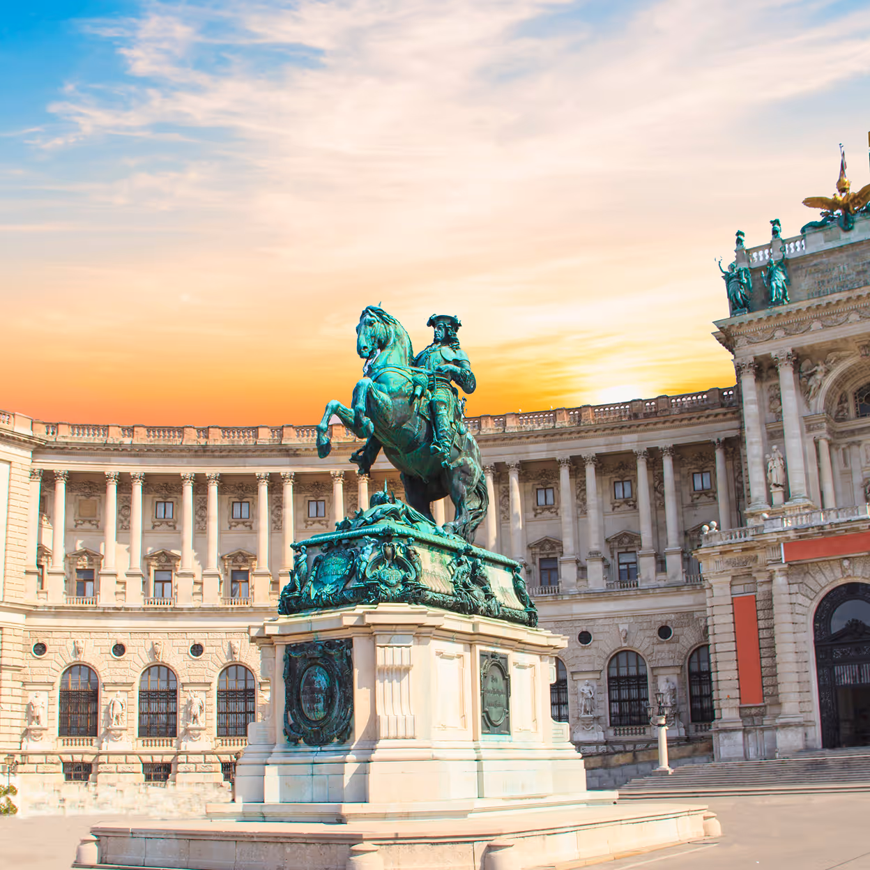 Reiterstatue vor historischer Säulenfassade bei Sonnenuntergang.