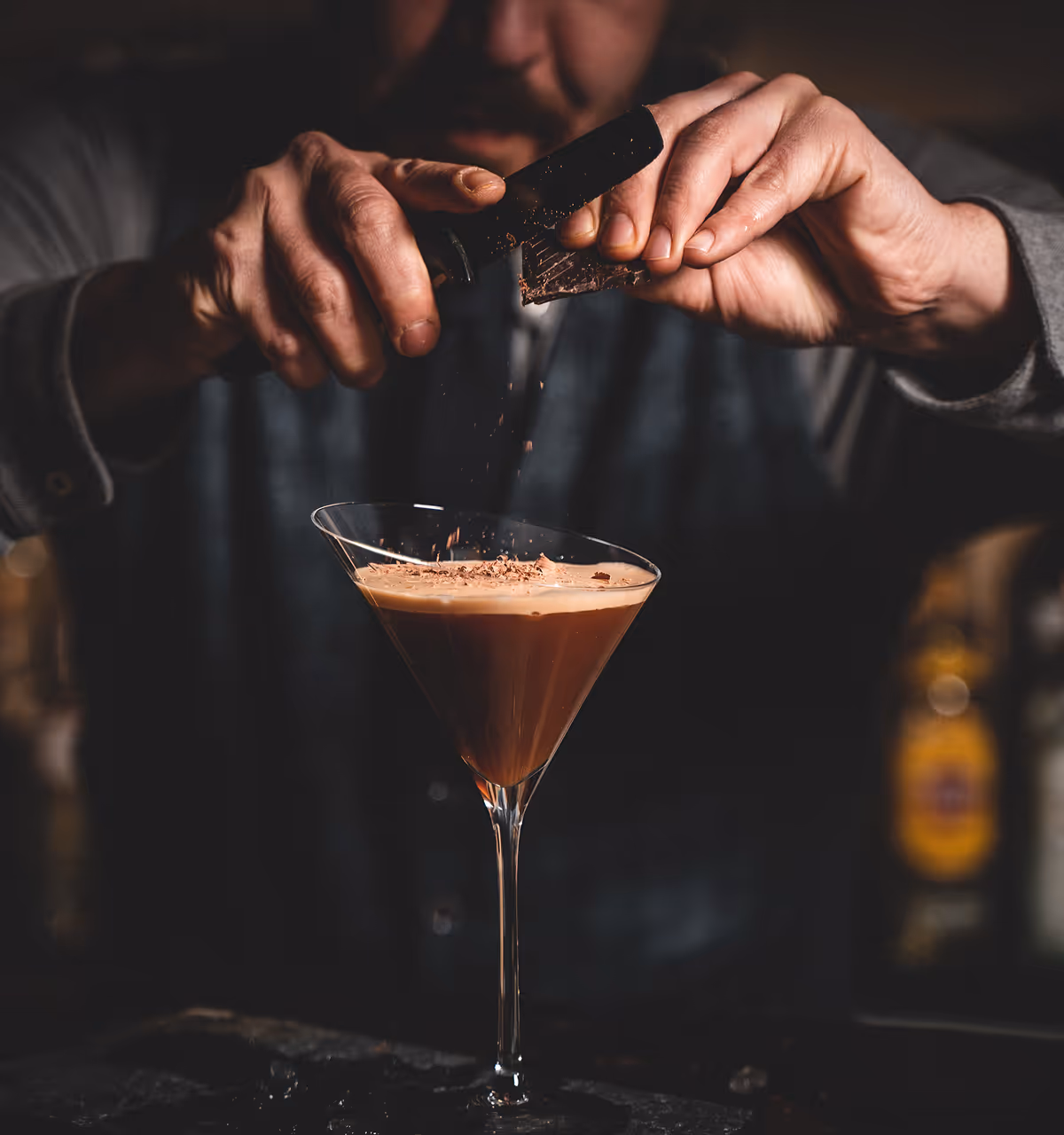 Eine Person raspelt Schokolade über einen Cocktail in einem Martini-Glas.