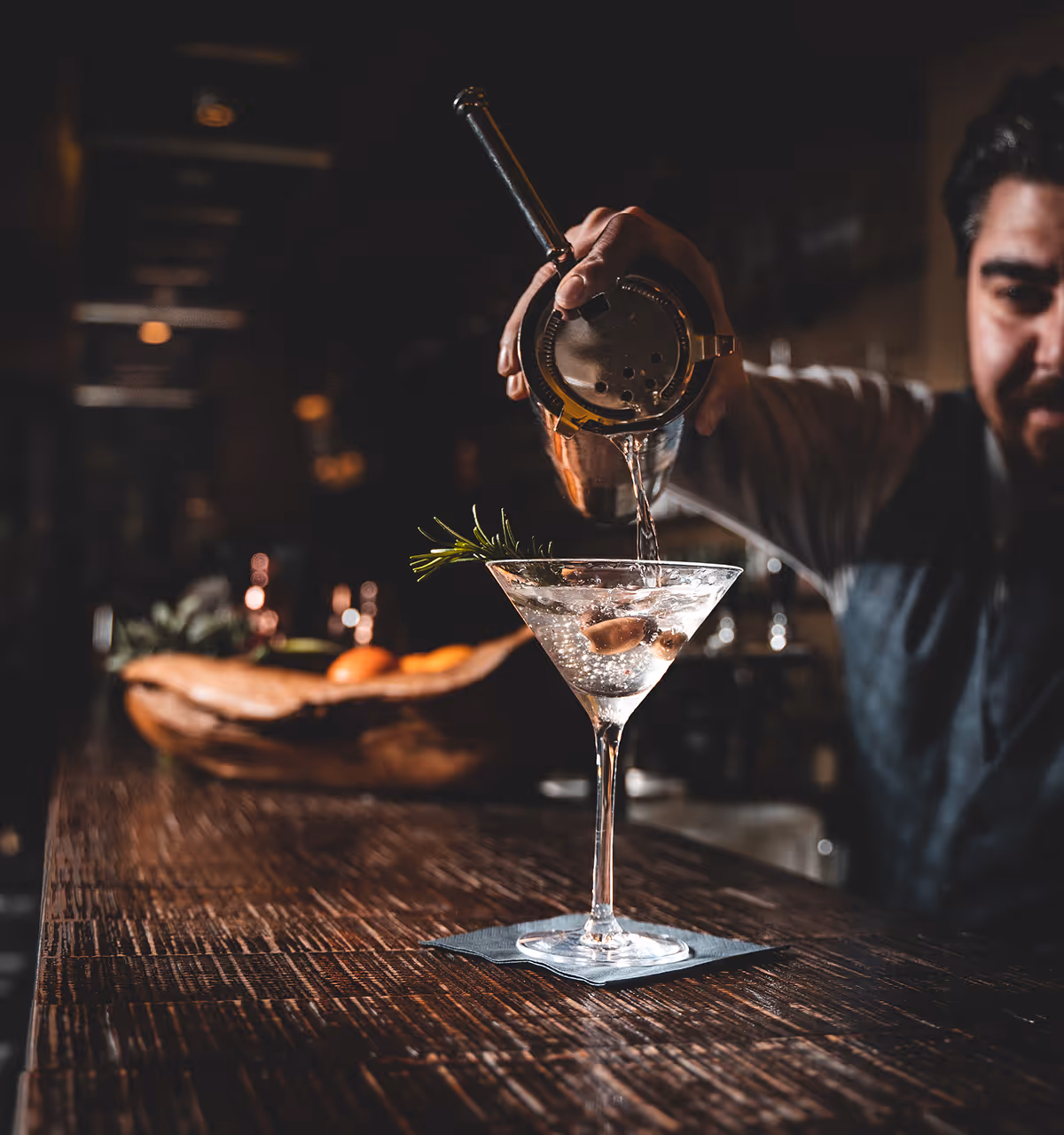 Barkeeper gießt einen Cocktail mit Rosmarinzweig in ein Martiniglas an einer Bar.