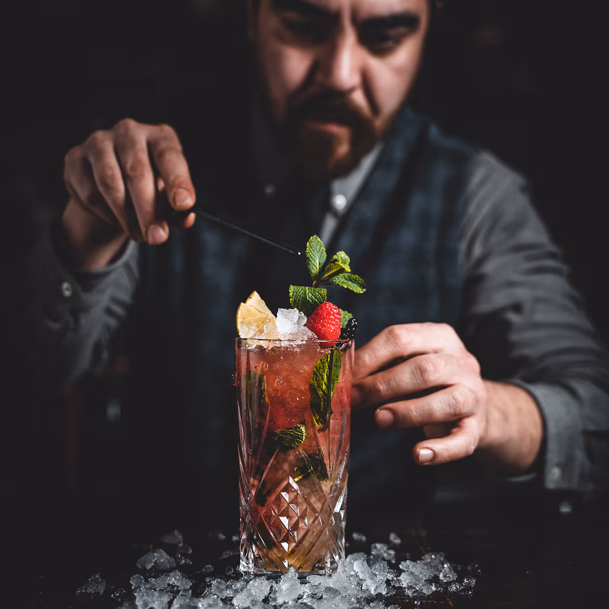 Barkeeper verziert einen mit Minze, Himbeere und Zitrone dekorierten Cocktail in einem Kristallglas.