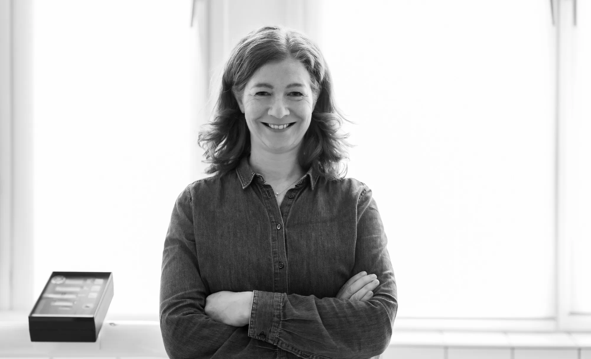 Schwarz-Weiß-Portrait von Jessica Mathiak mit verschränkten Armen, lächelnd in einem hellen Raum