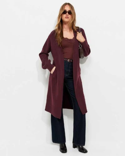 Model wearing a long burgundy cardigan, burgundy top and dark flared jeans
