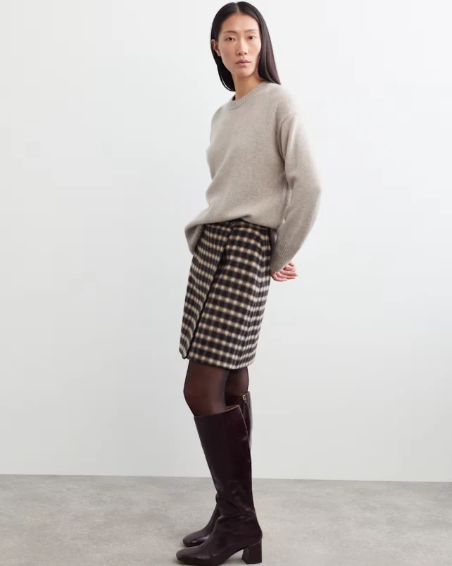 Model wearing an oatmeal knit jumper, checked mini skirt, dark tights and knee-high boots