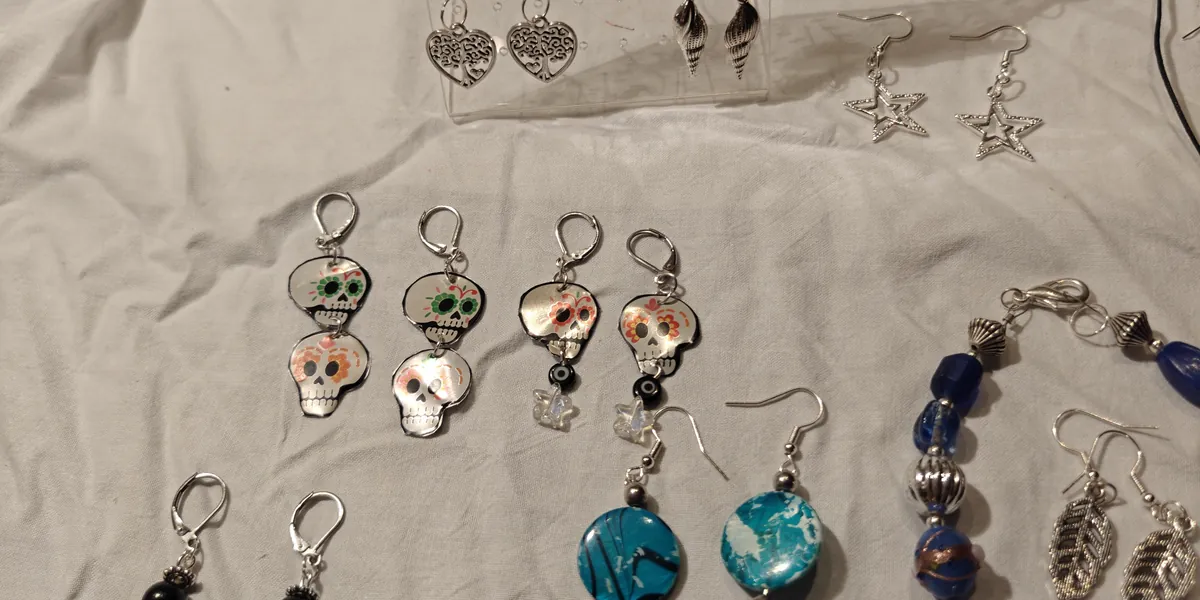 Handmade sugar skull earrings, silver star earrings and a blue beaded bracelet laid out on a white cloth