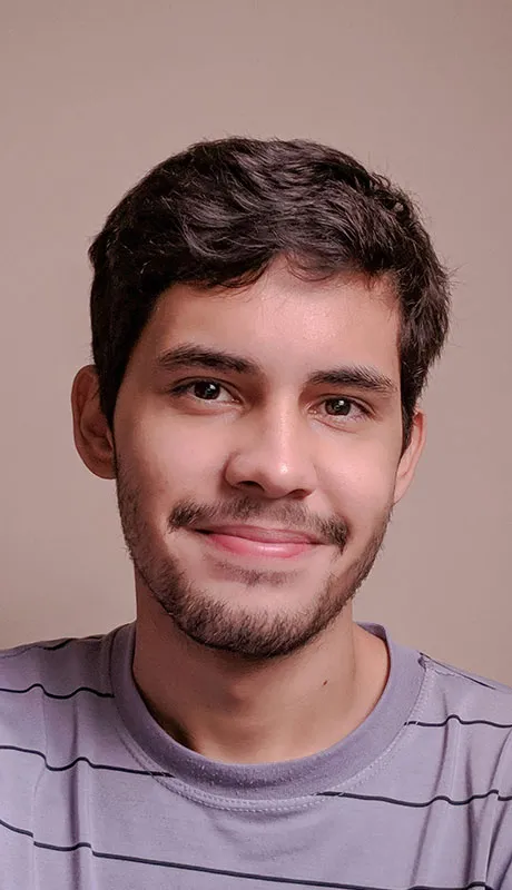 Young man with short dark hair and beard smiling wearing a striped gray shirt against a plain background.