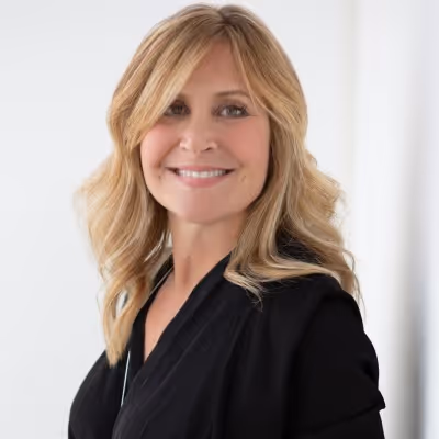 Smiling woman with blonde wavy hair wearing a black top against a white background.