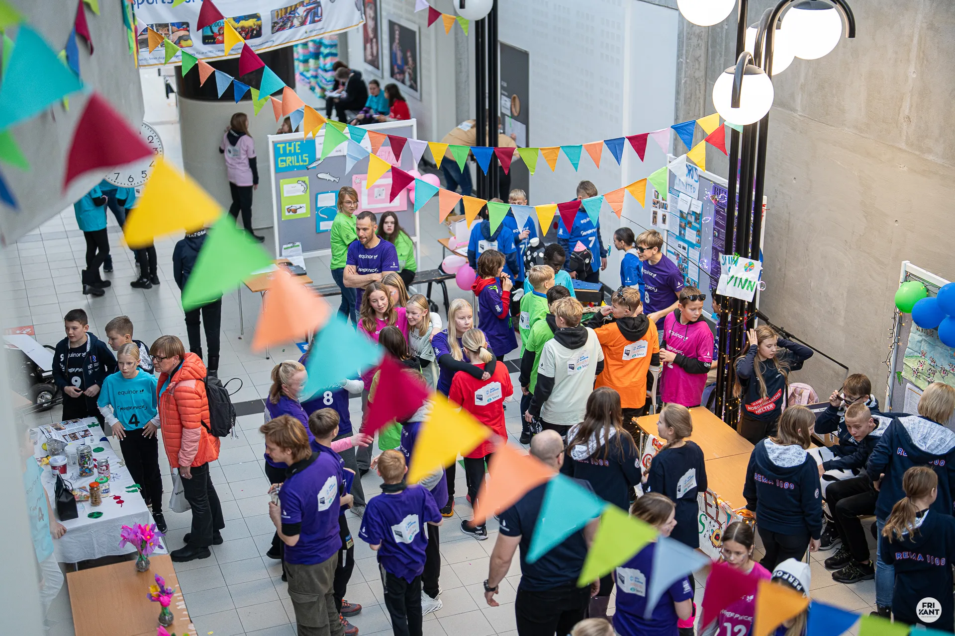 Ungdommer og voksne samles i en dekorert hall med fargerike vimpler og stands for et arrangement.