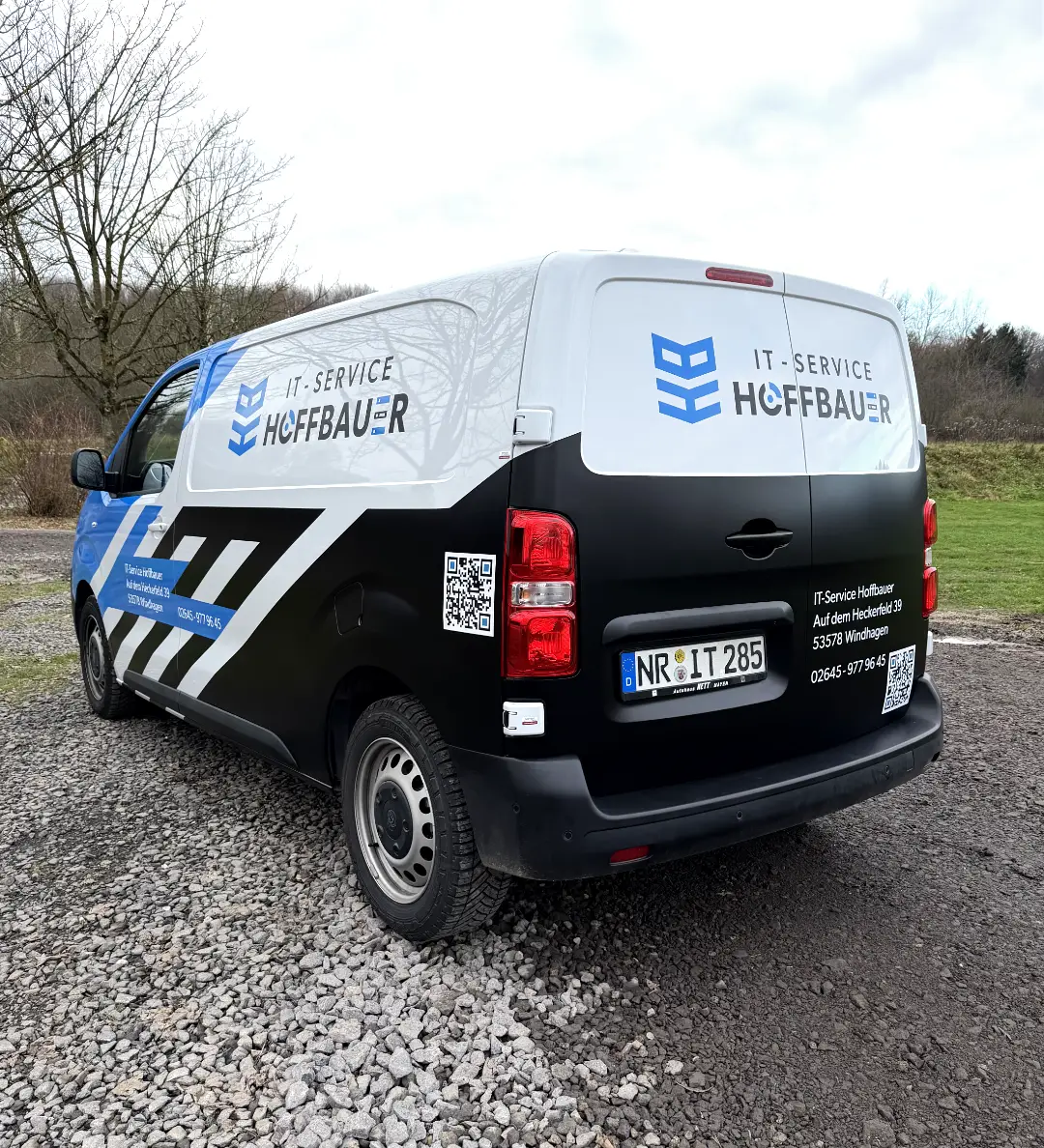 Dienstfahrzeug mit IT-Service Hoffbauer-Logo und Kontaktdaten, geparkt auf einem Schotterweg im Freien.