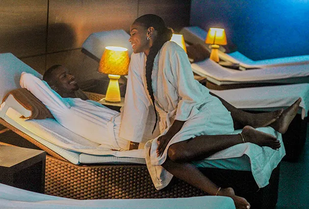 Un couple détendu assis sur un lit dans un spa, entouré d'une ambiance apaisante et de décorations relaxantes.