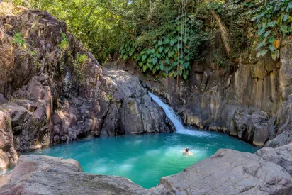 Cascade naturelle se jetant dans un bassin d’eau turquoise entouré de rochers et de végétation tropicale
