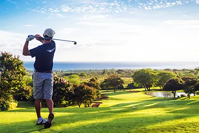 Golfeur en plein swing sur un parcours verdoyant avec vue panoramique sur l'océan, lors d'un séjour à La Créole Beach Hôtel & Spa.