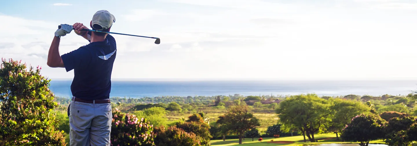 Golfeur en plein swing sur un parcours verdoyant avec vue panoramique sur l'océan, lors d'un séjour à La Créole Beach Hôtel & Spa.