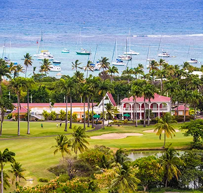 Vue panoramique depuis La Créole Beach Hôtel & Spa sur un parcours de golf verdoyant bordant un lagon turquoise parsemé de voiliers.