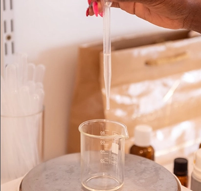 Atelier de création de parfum personnalisé à La Créole Beach Hôtel & Spa : une main utilisant une pipette pour doser une fragrance dans un bécher de précision.