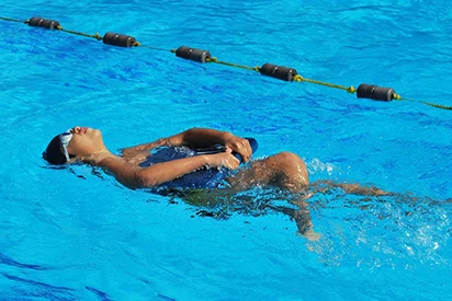 Enfant apprenant à nager sur le dos avec une planche de flottaison dans la piscine de La Créole Beach Hôtel & Spa.