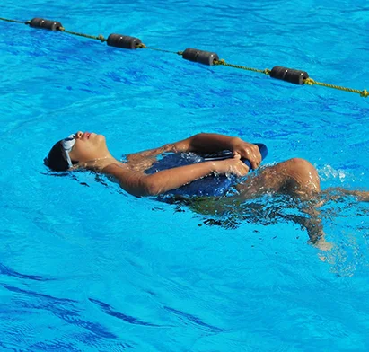 Enfant apprenant à nager sur le dos avec une planche de flottaison dans la piscine de La Créole Beach Hôtel & Spa.