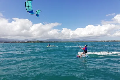 Kitesurf en mer face à La Créole Beach Hôtel & Spa sous un ciel nuageux.