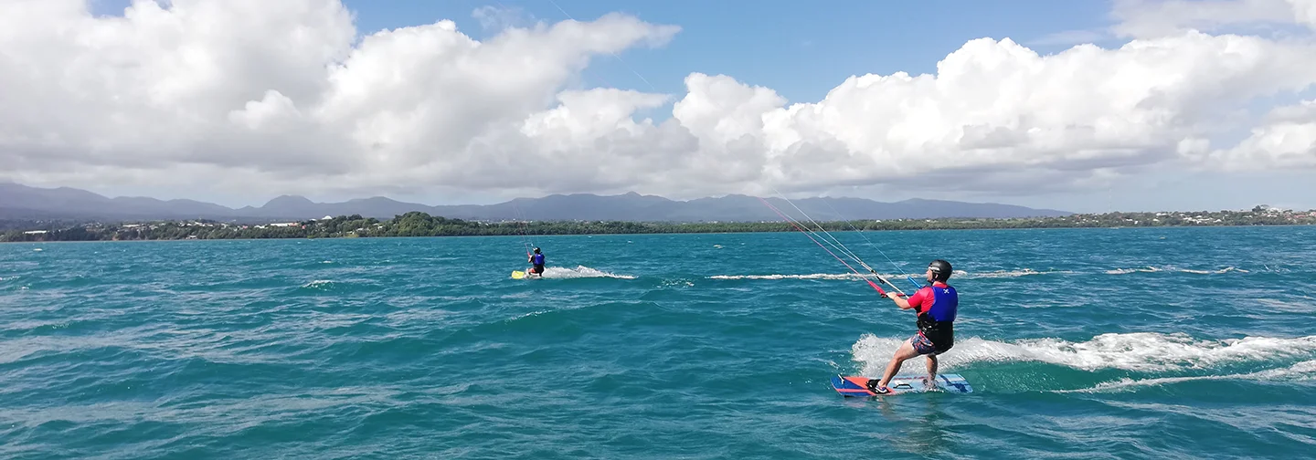 Kitesurf en mer face à La Créole Beach Hôtel & Spa sous un ciel nuageux.