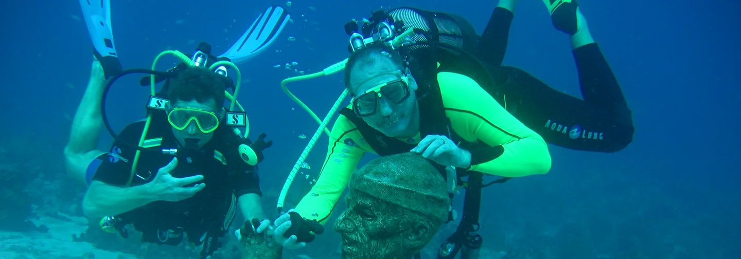 Deux plongeurs explorant la statue sous-marine de Jacques Cousteau en Guadeloupe, une activité proposée par La Créole Beach Hôtel & Spa.