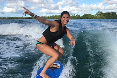 Une femme souriante pratiquant le wake surf sur une eau turquoise à La Créole Beach Hôtel & Spa.