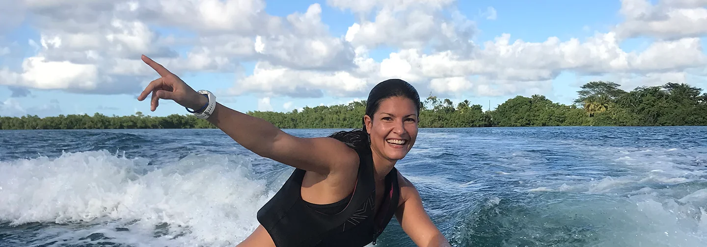 Une femme souriante pratiquant le wake surf sur une eau turquoise à La Créole Beach Hôtel & Spa.