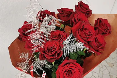 Vue de dessus d'un bouquet confectionné de 12 roses rouges fraîches et éclatantes, entourées d'un emballage décoratif.