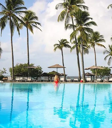 Großer tropischer Pool, umgeben von Palmen und Sonnenschirmen mit Blick auf das Karibische Meer im Luxushotel La Créole Beach Hotel & Spa in Le Gosier, Guadeloupe.
