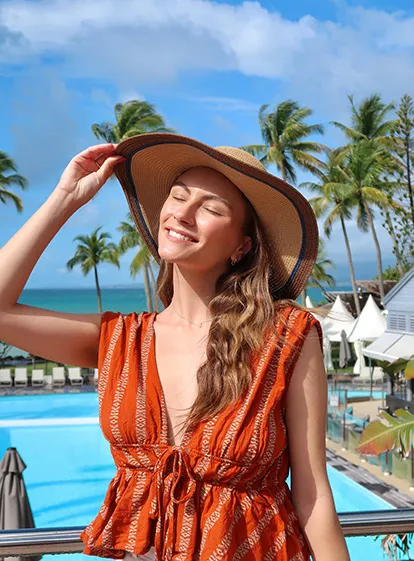 Lächelnde Frau mit Strohhut vor einem tropischen Pool im La Créole Beach Hotel & Spa in Le Gosier.