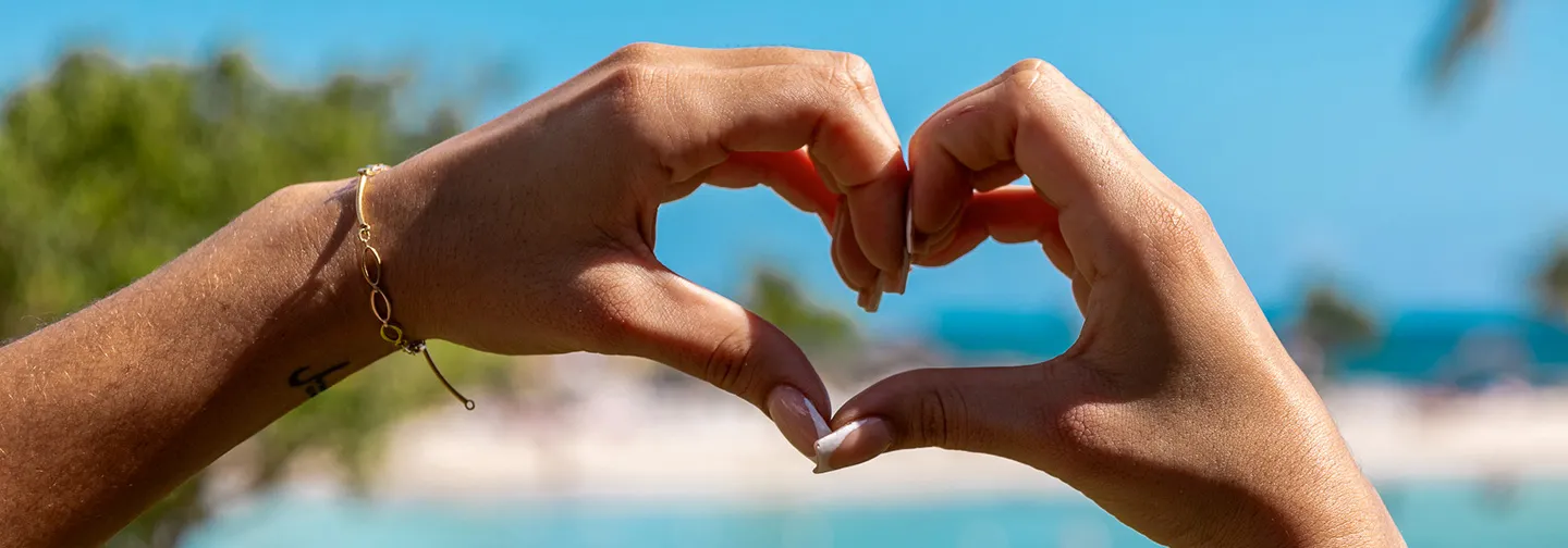 Heart-shaped hands in front of a tropical beach and the Caribbean Sea.