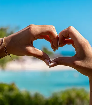 Heart-shaped hands in front of a tropical beach and the Caribbean Sea.