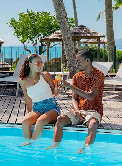 Couple enjoying a friendly moment with cocktails by the pool at the 4-star hotel La Créole Beach Hotel & Spa in Gosier, Guadeloupe.